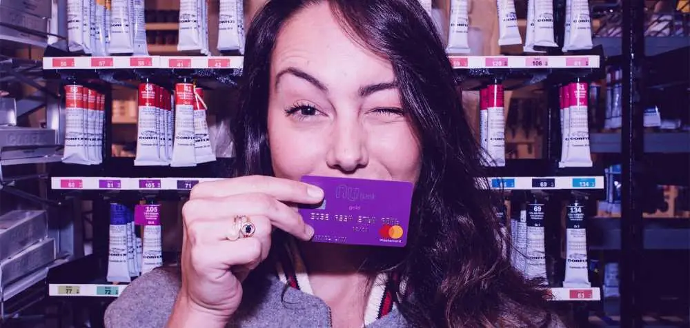 mulher segurando cartão de crédito do Nubank, piscando um olho
