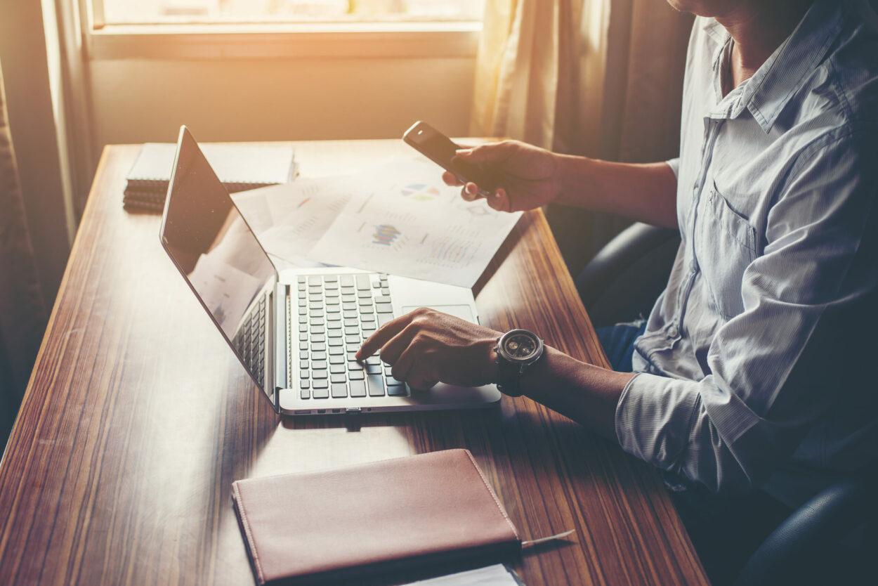 Vendas por whatsapp: homem digitando no notebook e mexendo no celular