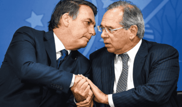 Presidente da República, Jair Bolsonaro à esquerda, e Minsitro da Economia, Paulo Guedes, à direita. Ambos estão ao lado um do outro, e com as mãos dadas