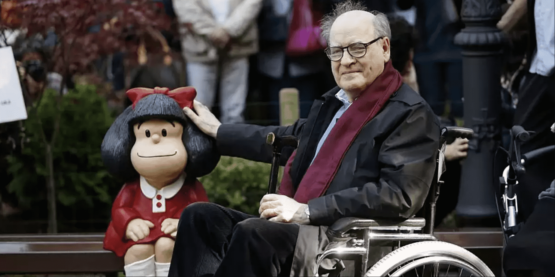 Foto mostra Quino ao lado de uma escultura da Mafalda