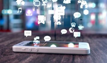 celular deitado na mesa com ícones flutuantes de redes sociais