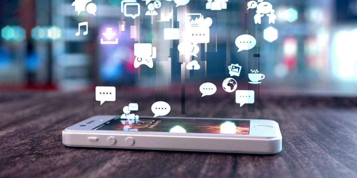 celular deitado na mesa com ícones flutuantes de redes sociais