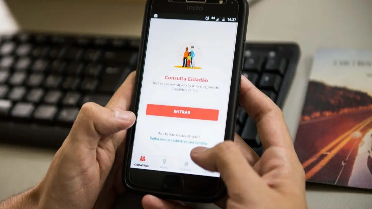Homem segurando o celular aberto no aplicativo Meu CadÚnico para realizar consulta