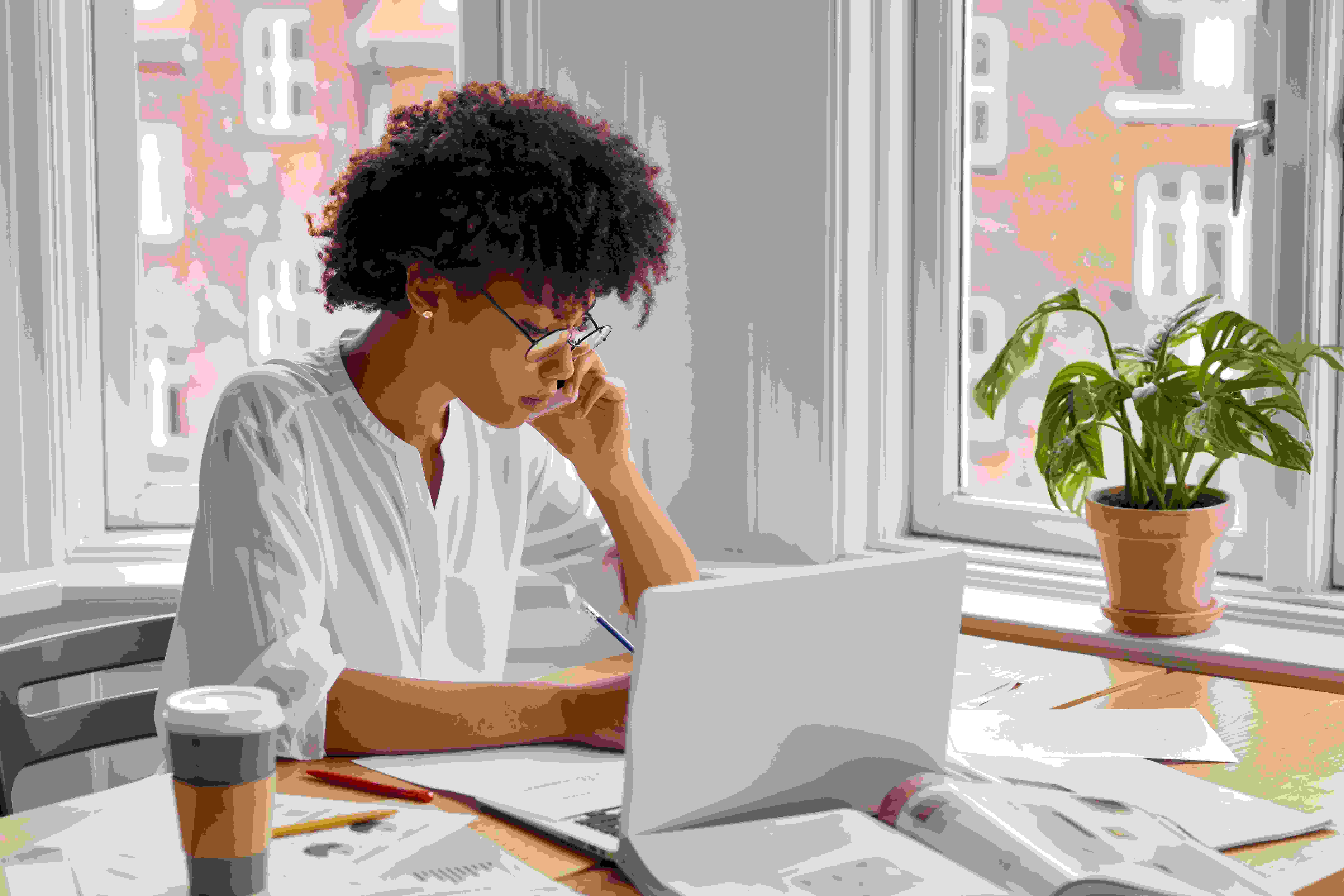 Mulher sentada de frente a um notebook branco, falando ao telefone e fazendo anotações sobre contrato social MEI