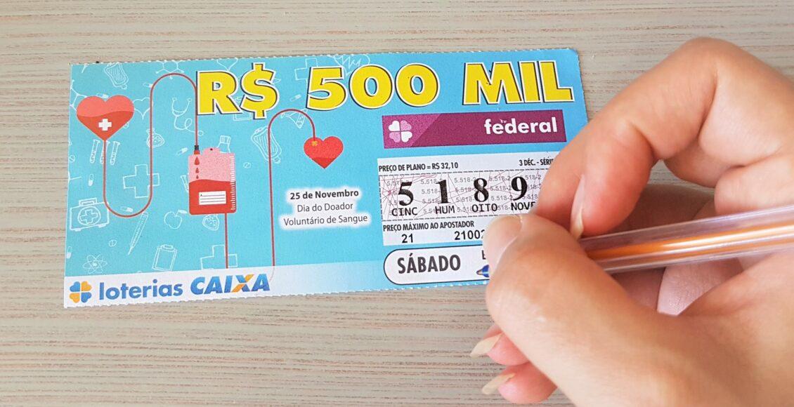 A imagem mostra uma mão segurando uma caneta e um bilhete da loteria Federal 5521