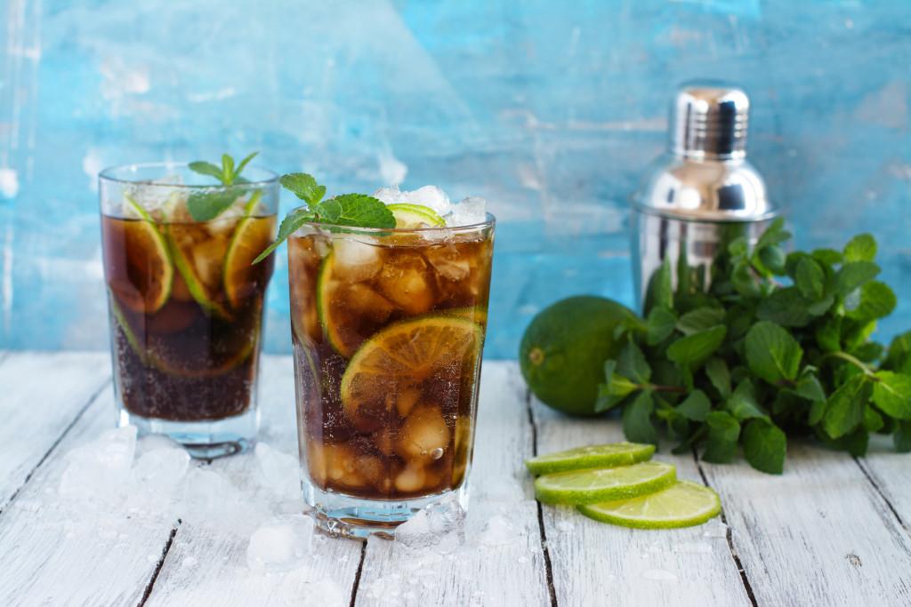 Foto mostra copo de cuba, ao lado uma coqueteleira e limão - receitas de drink