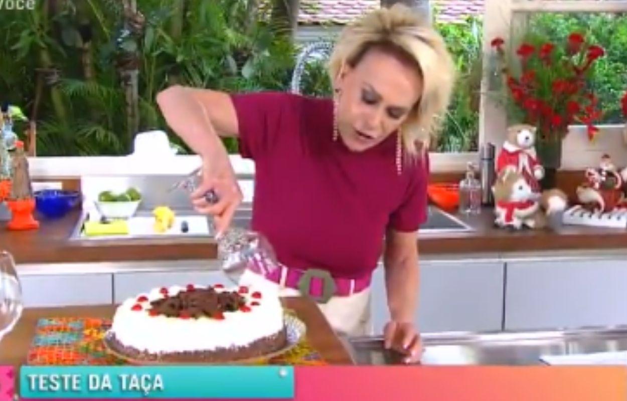 Imagem mostra Ana Maria Braga cortando bolo com a taça