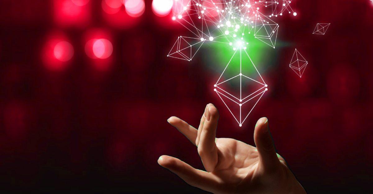 Mão segurando logotipo da ETH 2.0, nova rede Ethereum, em fundo vermelho