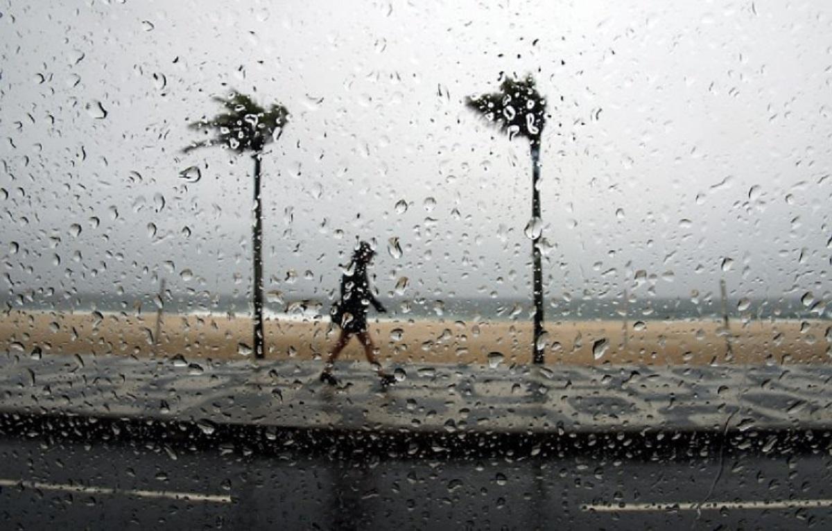 Previsão do tempo no litoral: homem anda na chuva na orla da praia