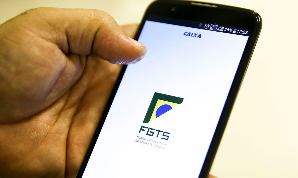 Foto mostra mãos masculinas segurando celular aberto em página do FGTS, da Caixa Econômica Federal.