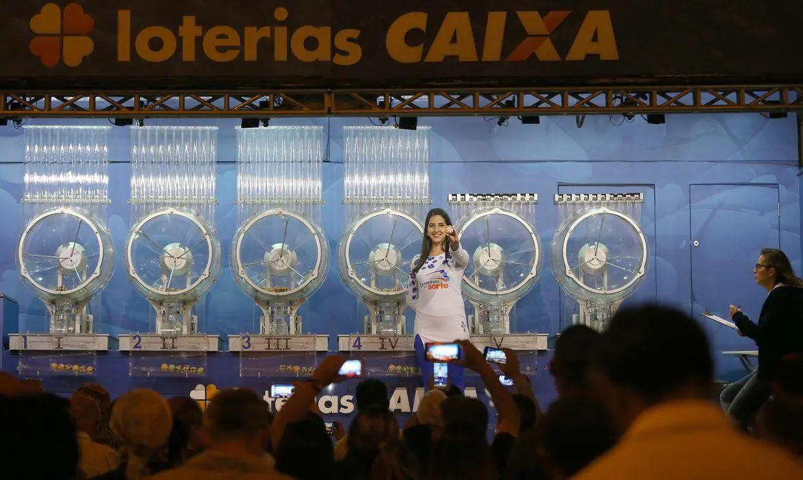 A imagem mostra uma mulher segurando uma bola de número sorteado