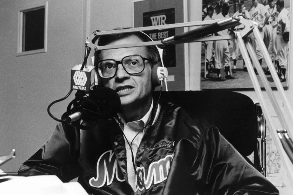 Imagem preta e branca do jornalista Larry King. Ele está segurando um microfone