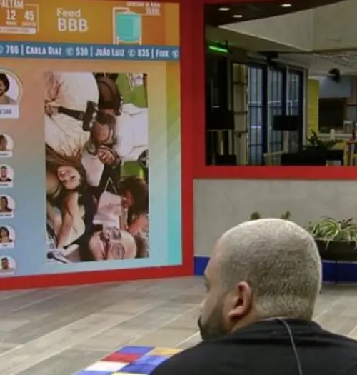 Na imagem Projota observa João em telão na sala do BBB21