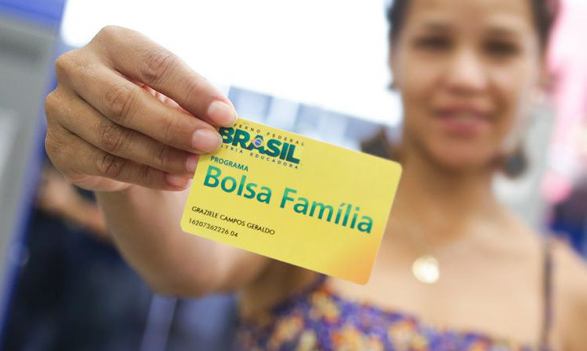 Foto mostra mulher segurando cartão do Bolsa Família