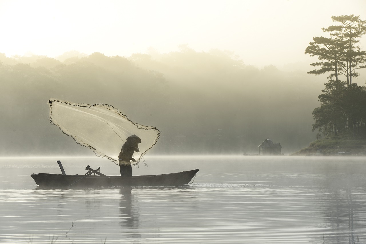 Foto mostra pescador sobre barco em meio ao mar atirando rede de pesca.