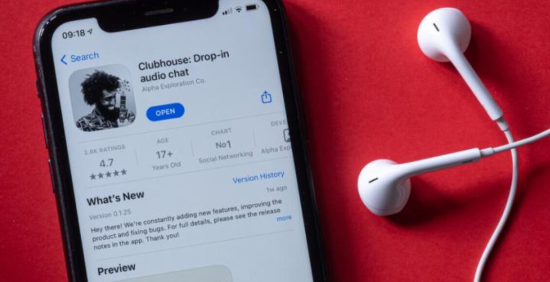 Imagem mostra celular e fone de ouvidos. Tela do aparelho exibe aplicativo Clubhouse