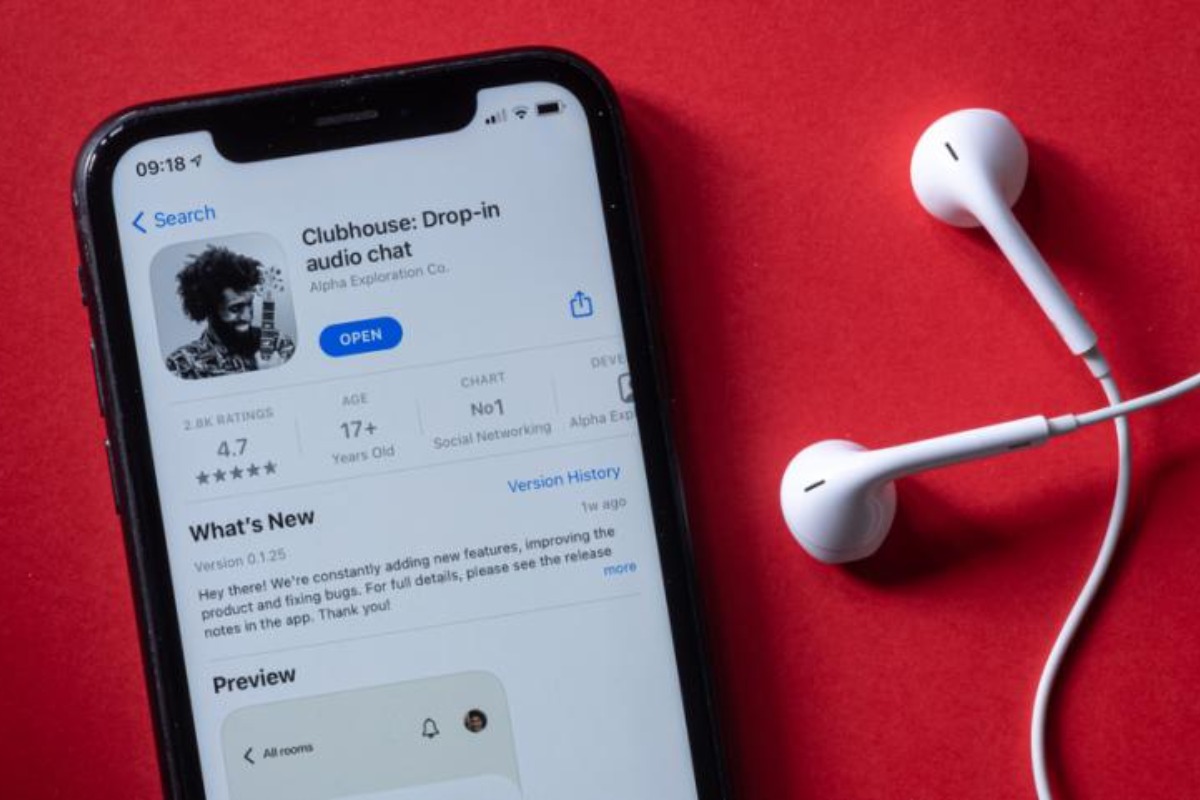 Imagem mostra celular e fone de ouvidos. Tela do aparelho exibe aplicativo Clubhouse