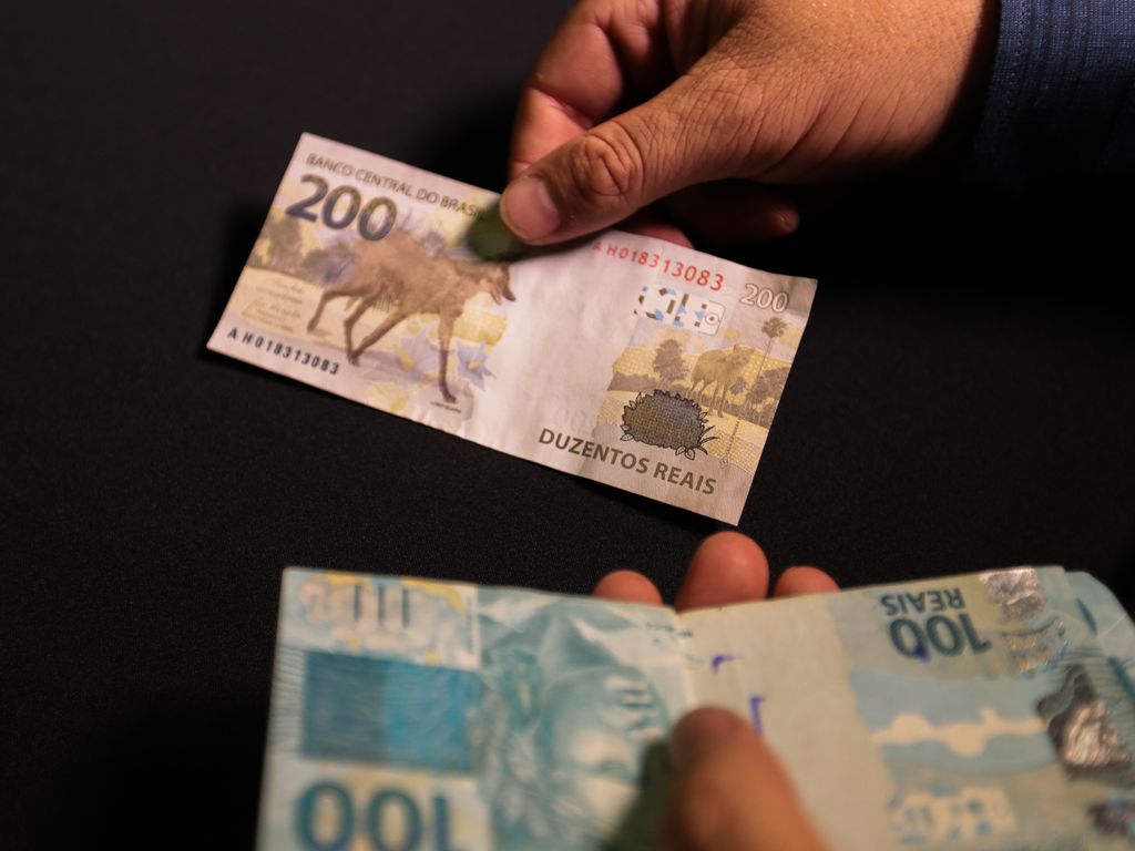Foto mostra homem segurando notas de 200 e 100 reais.