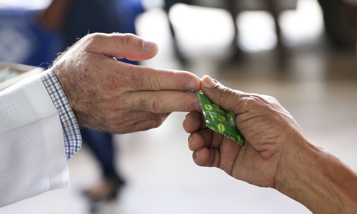 na foto, uma pessoa entrega um preservativo para outra. esse objeto é usado para reduzir a transmissão do vírus HIV e, consequentemente, reduzir chances de alguém ter a aids