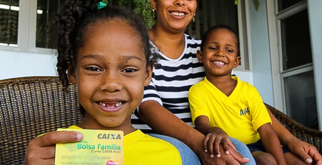 Uma família sorridente exibe o seu cartão do Bolsa Família