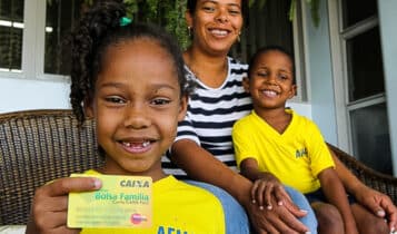 Uma família sorridente exibe o seu cartão do Bolsa Família